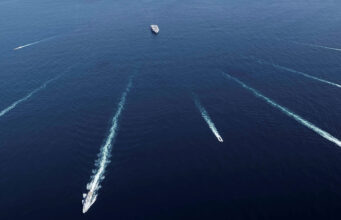 Aerial view of several ships at sea leaving white wake trails that intersect on the deep blue ocean.