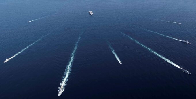 Aerial view of several ships at sea leaving white wake trails that intersect on the deep blue ocean.