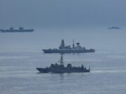 British carrier group encounters Russian spy ship Formation of three gray warships sailing on a calm blue sea with a hazy horizon.