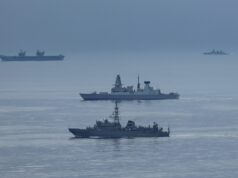 British carrier group encounters Russian spy ship Formation of three gray warships sailing on a calm blue sea with a hazy horizon.
