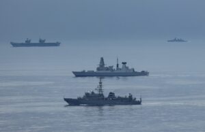 British carrier group encounters Russian spy ship Formation of three gray warships sailing on a calm blue sea with a hazy horizon.