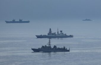 British carrier group encounters Russian spy ship Formation of three gray warships sailing on a calm blue sea with a hazy horizon.