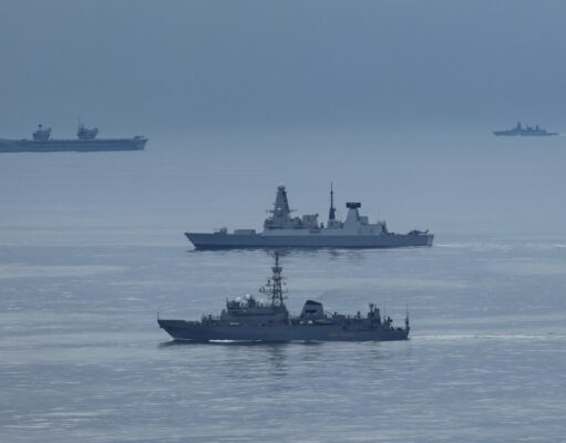 British carrier group encounters Russian spy ship Formation of three gray warships sailing on a calm blue sea with a hazy horizon.