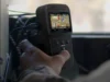 Handheld GPS device displaying a color map, held by a person in a vehicle cockpit