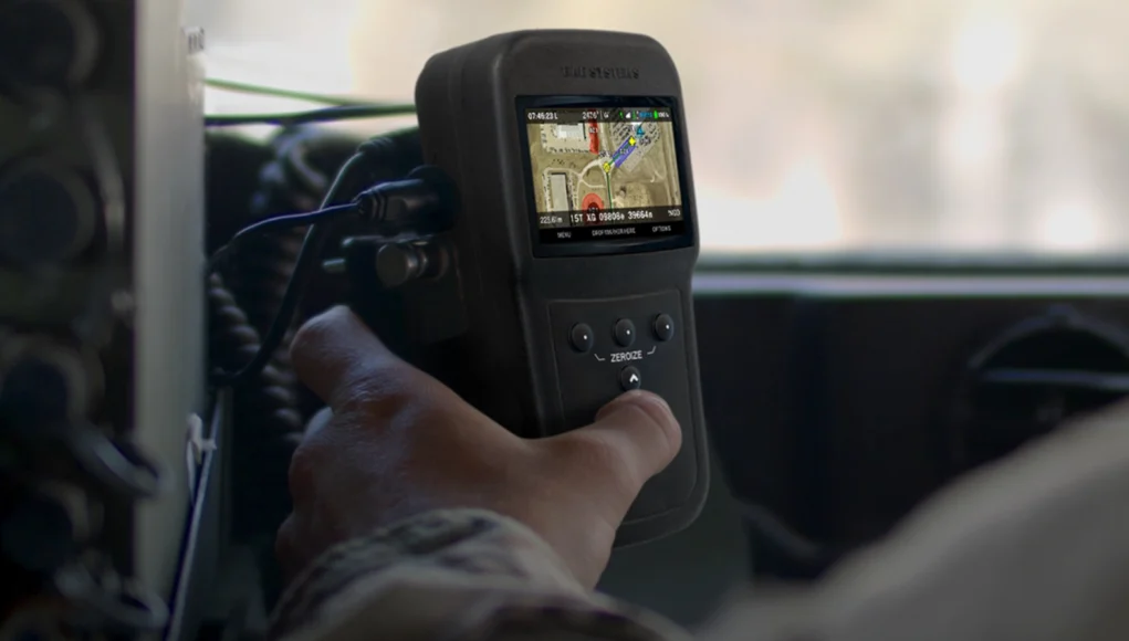 Handheld GPS device displaying a color map, held by a person in a vehicle cockpit
