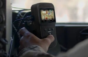 Handheld GPS device displaying a color map, held by a person in a vehicle cockpit