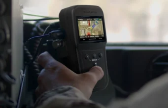Handheld GPS device displaying a color map, held by a person in a vehicle cockpit