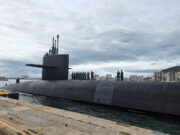 US nuclear missile sub in port call to British territory Submarine moored at the quay with crew on its deck and a city skyline in the background.