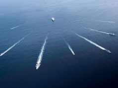 Aerial view of several motorboats leaving white wake trails across deep blue ocean surface (six boats visible).