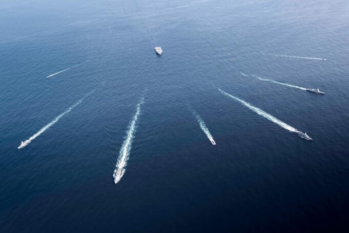 Aerial view of several motorboats leaving white wake trails across deep blue ocean surface (six boats visible).