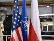 US and Poland complete deployable air base storage site Flags of the United States, NATO, and Poland in front of military trucks inside a warehouse or hangar.