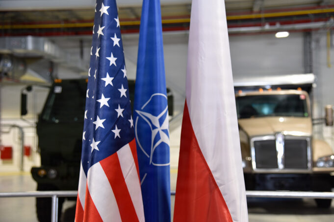 US and Poland complete deployable air base storage site Flags of the United States, NATO, and Poland in front of military trucks inside a warehouse or hangar.