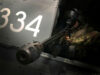 Military helicopter side with large white '334' numbers and a crewman in camouflage sitting at a mounted gun in the open hatch, aiming outward.