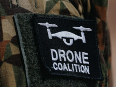 The NATO Innovation Badge Close-up of a black Velcro patch with a white winged emblem on camouflage military uniform.