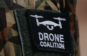 Close-up of a black Velcro patch with a white winged emblem on camouflage military uniform.
