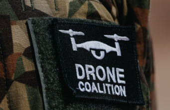 Close-up of a black Velcro patch with a white winged emblem on camouflage military uniform.