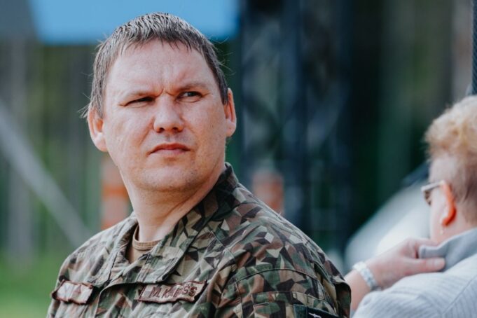 Latvia drone range pushing NATO industry to meet reality Man in camouflage military uniform looking left outdoors, with another person partially visible.