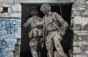 Grenadier Guards drill in abandoned Cyprus village Two soldiers in full combat gear exit a ruined stone building, rifles at the ready.