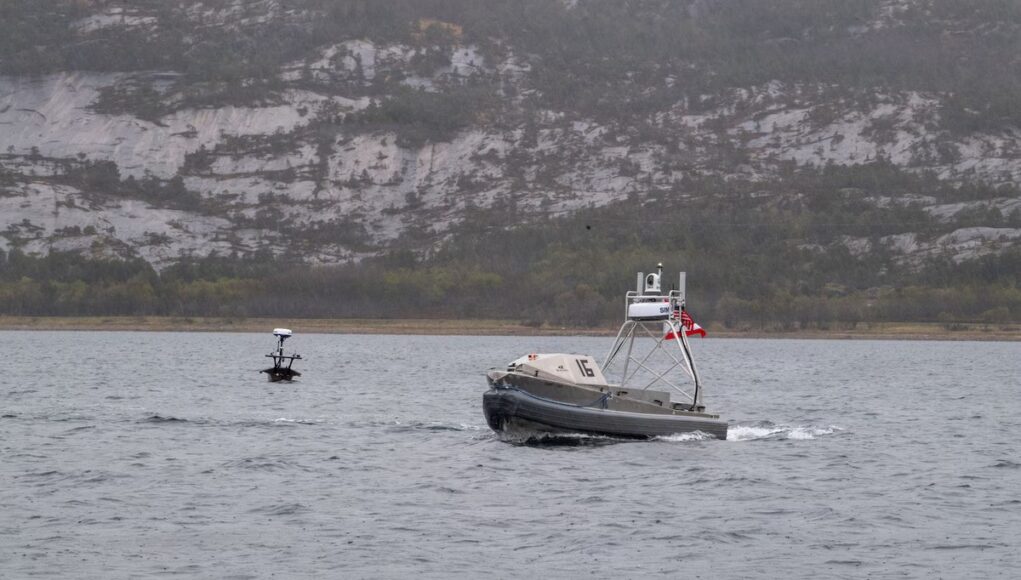 AMERICASTUFF Metal patrol boat with the number 16 speeds across the water, with a rocky hillside in the distance.