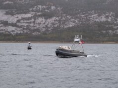 U.S. Navy tests unmanned systems in Arctic exercise Metal patrol boat with the number 16 speeds across the water, with a rocky hillside in the distance.