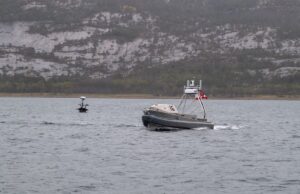 U.S. Navy tests unmanned systems in Arctic exercise Metal patrol boat with the number 16 speeds across the water, with a rocky hillside in the distance.