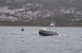 U.S. Navy tests unmanned systems in Arctic exercise Metal patrol boat with the number 16 speeds across the water, with a rocky hillside in the distance.