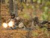 Soldiers in camouflage firing a light machine gun in a forest, muzzle flash brightening the scene.
