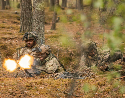 Soldiers in camouflage firing a light machine gun in a forest, muzzle flash brightening the scene.