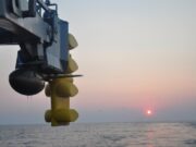 Canada picks Thales S2087 sonar for River-class ships Close-up of a blue offshore platform component with yellow stabilizers hanging over a calm sea at sunset.