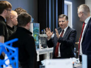 Alexander hails King’s Speech defence commitments Group of professionals in a lab, a suited man explaining with hands raised to colleagues gathered around equipment.
