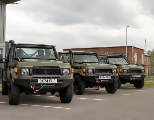 Row of olive green military-style Jeeps parked in a lot outside a building under a cloudy sky, front view shows license plates BX74 FLD and BX74 FEK.