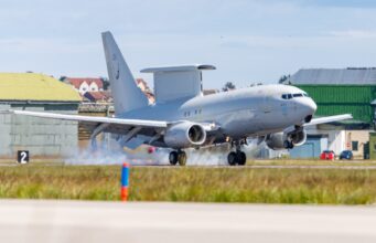 New Wedgetail early warning aircraft arrives at Lossiemouth RAF transport aircraft lifting off from runway at an airbase with hangars and buildings in the background