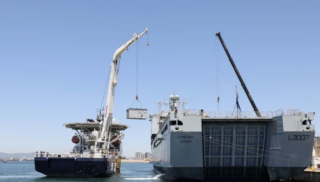 FLEET-20260520-XH0035-007 Two large ships at a harbor with cranes lifting a container between them, likely a transfer operation at sea.