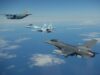 NATO fighters intercept Russian strike jet over Baltic Three military aircraft in formation over the ocean with scattered clouds beneath them.