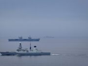 Destroyer joins aircraft carrier for Nordic deployment Large gray naval warship in the foreground on calm water, with smaller ships visible on the horizon (hull marked D37).