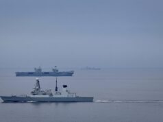Destroyer joins aircraft carrier for Nordic deployment Large gray naval warship in the foreground on calm water, with smaller ships visible on the horizon (hull marked D37).
