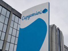 Capgemini corporate sign with blue curved graphic on a tall white panel beside a glass-front building exterior