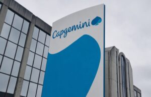 Capgemini corporate sign with blue curved graphic on a tall white panel beside a glass-front building exterior