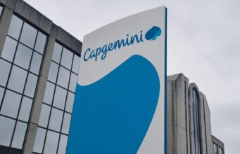 Capgemini corporate sign with blue curved graphic on a tall white panel beside a glass-front building exterior
