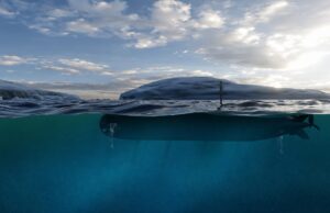 BAE and Thales expand ambitions for Herne XLAUV Submarine partially submerged with the hull just below the surface and a periscope rising above the water under a cloudy sky.