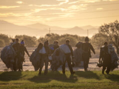 RAF parachute test team completes 500 jumps in Arizona Group of skydivers in full gear and parachutes walking together across a field at sunset with mountains in the distance at the horizon.
