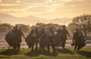 RAF parachute test team completes 500 jumps in Arizona Group of skydivers in full gear and parachutes walking together across a field at sunset with mountains in the distance at the horizon.