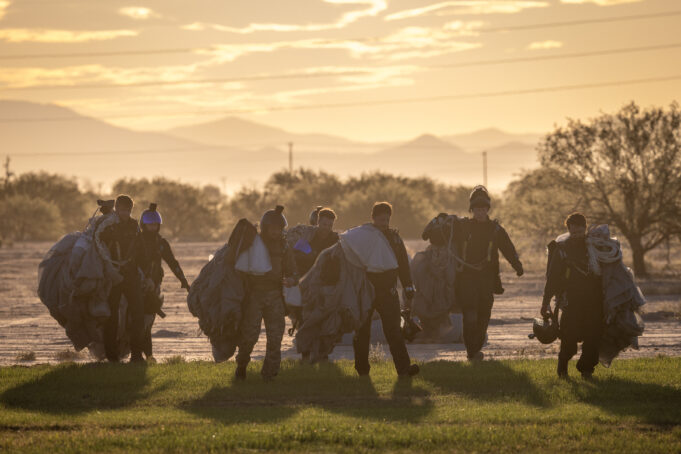 RAF parachute test team completes 500 jumps in Arizona Group of skydivers in full gear and parachutes walking together across a field at sunset with mountains in the distance at the horizon.