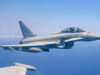 Royal Air Force Eurofighter Typhoon in flight over the sea, with underwing weapons and drop tanks visible.