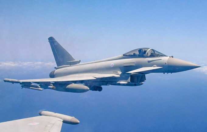 Royal Air Force Eurofighter Typhoon in flight over the sea, with underwing weapons and drop tanks visible.