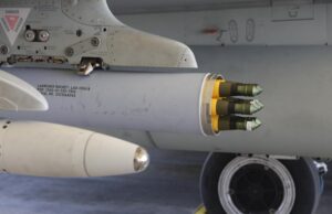 Close-up of a wing-mounted rocket launcher under a military aircraft, showing yellow-tipped missiles ready for launch