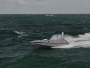 Gray speedboat racing across choppy dark green ocean with white spray at the stern, under a cloudy sky.