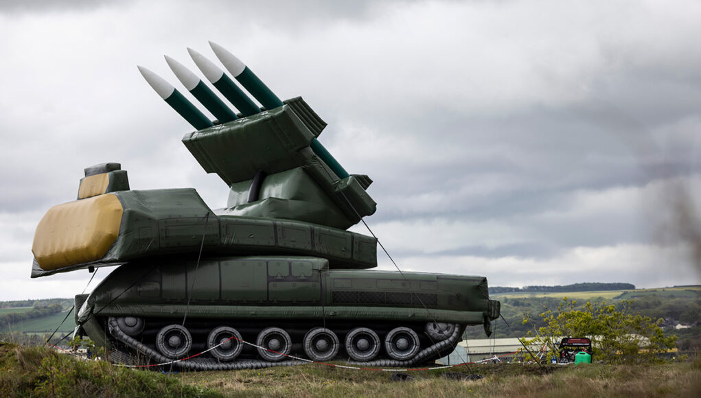 LEE-20260513-0172-Draken_STING_Demo-0051 Large green mobile missile launcher with four missiles raised on a field under a cloudy sky.