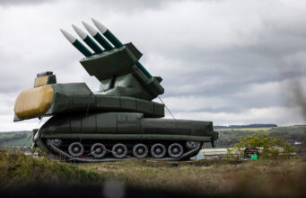 Large green mobile missile launcher with four missiles raised on a field under a cloudy sky.