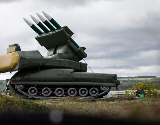 Large green mobile missile launcher with four missiles raised on a field under a cloudy sky.